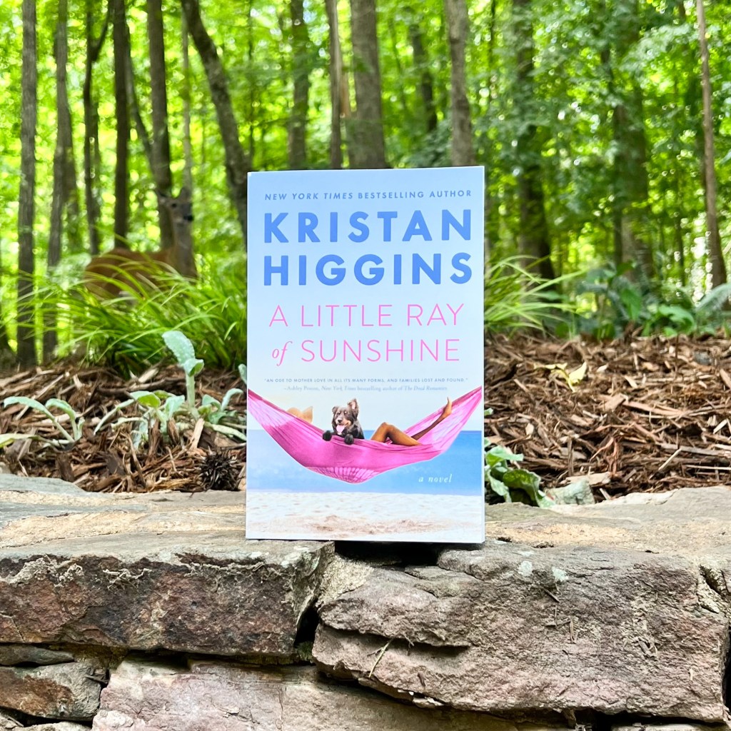 Photo of Kristan Higgin's A Little Ray of Sunshine paperback on rock ledge surrounded by trees